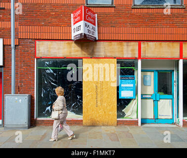 Femme marche passé boutique vide, Barrow-in-Furness Cumbria, Angleterre, Royaume-Uni Banque D'Images