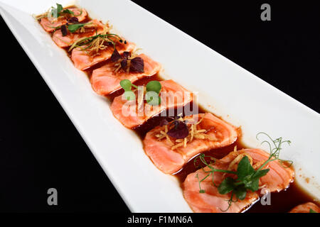 Pavé de saumon avec la sauce et la décoration de légumes en plaque blanche sur fond noir Banque D'Images