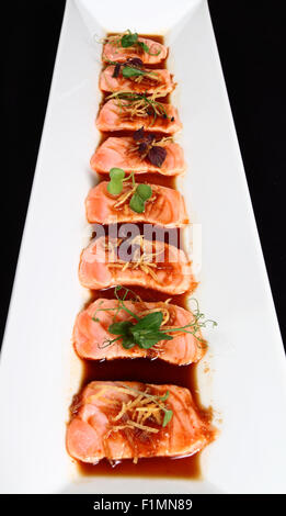 Pavé de saumon avec la sauce et la décoration de légumes en plaque blanche sur fond noir Banque D'Images