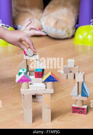 Close-up of a little girl's hand construire quelque chose à l'aide de pièces géométriques en bois, dans sa salle de jeu. Banque D'Images