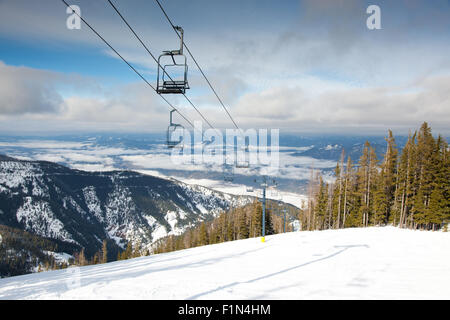 Un remonte-pente qui monte une montagne escarpée couverte de neige fraîche et une vallée derrière avec brouillard matinal. Banque D'Images