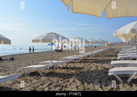 Transats et parasols sur la plage de Playa San Juan, Alicante, avec des gens qui arrivent à la plage tôt le matin. Banque D'Images