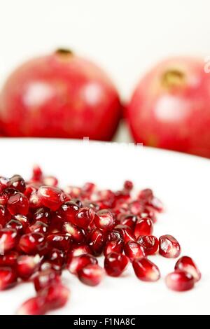 Régime alimentaire de grenade. Graines de Grenade bio frais sur plaque blanche et les fruits entiers en arrière-plan. Banque D'Images