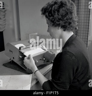 Historique, 1950, photo montrant une femme secrétaire ou greffier ou l'assistant des comptes au travail à l'aide d'une petite machine d'impression. Banque D'Images