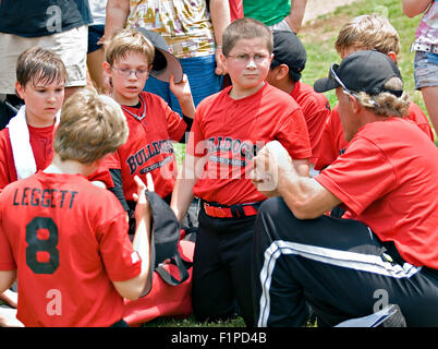 Un coach parle à son équipe de baseball de la petite ligue, les familles sont dans l'arrière-plan l'écoute. Banque D'Images