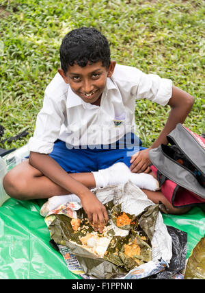 School-boy Eating Lunch au Jardin botanique royal de Peradeniya, près de Kandy, Sri Lanka Banque D'Images