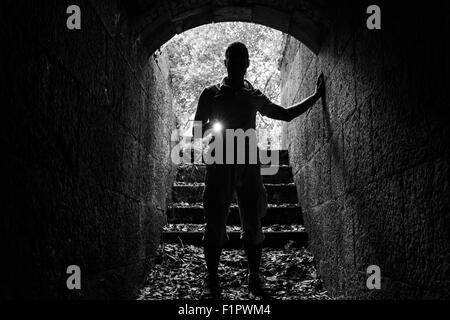 Jeune homme avec une lampe de pierre entre dans le tunnel et regarde dans l'obscurité, photo monochrome Banque D'Images