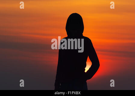 Silhouette de la jeune fille dans les vêtements de sport avec une capuche au coucher du soleil Banque D'Images