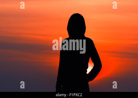 Silhouette de la jeune fille dans les vêtements de sport avec une capuche au coucher du soleil Banque D'Images