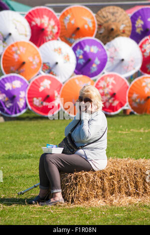 Poole, Dorset, UK. 6 Septembre, 2015. Poole Festival thaïlandais s'est imposé comme l'un des plus populaires du Festival thaïlandais dans le pays. Woman on phone sitting on hay bale avec parasols colorés derrière Crédit : Carolyn Jenkins/Alamy Live News Banque D'Images