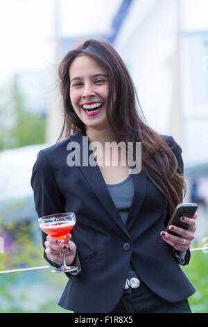 Jeune femme brunette latino-américaine/latine souriante, avec un téléphone portable et un verre Banque D'Images