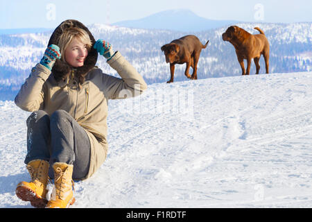 Femme assise sur un champ de neige avec ses chiens contre les montagnes au loin sur une journée ensoleillée d'hiver. Jouer, Dog Training, bonheur, va Banque D'Images