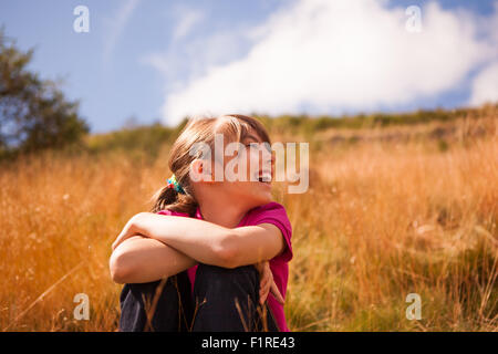 Jolie jeune fille assise sur une banque de l'herbe en riant sur un jour lumineux Banque D'Images