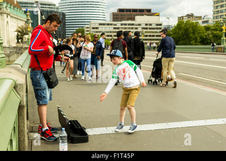 18 Août - Musicien ambulant joue le pont de Westminster, près de Big Ben en tant que professionnels prendre soin enfant jette des pièces de monnaie dans son cas Banque D'Images