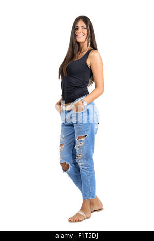 Belle jeune femme en jeans déchirés smiling at camera avec les mains dans les poches. Full body isolated over white Banque D'Images