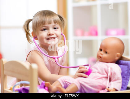 Enfant jouant le rôle médecin examinating jeu sa poupée à l'aide de stéthoscope assis dans une salle de jeux à la maison, à l'école ou au jardin d'enfants Banque D'Images