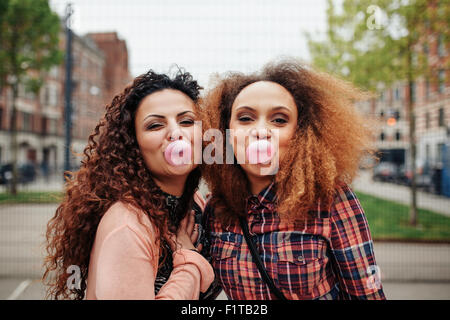 Heureux les jeunes femmes blowing bubble gum. Meilleurs amis de mâcher de la gomme, à l'extérieur. Banque D'Images