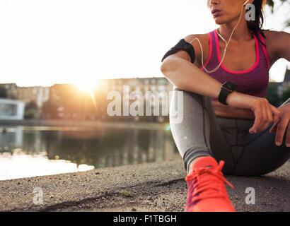 Jeune femme runner se reposant après séance d'entraînement sur matin ensoleillé. Modèle de remise en forme féminine assise sur le long de la rue de l'étang ville. Fe Banque D'Images