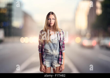 Trois quart tourné d'un jeune Blond Woman Wearing Trendy Robe courte Denim avec chemise manches longues à carreaux debout sur un st Banque D'Images