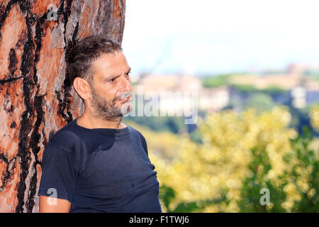 Young man leaning on tree trunk à l'extérieur en tirer Banque D'Images