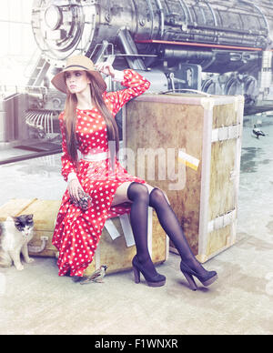 La fille assise sur la valise en attente à la gare ferroviaire de retro Banque D'Images