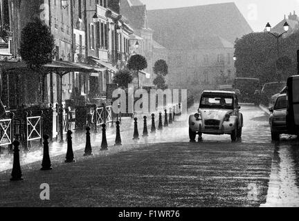 Scène de rue français Classic 2CV Citroën voiture roulant le long d'une rue dans de fortes pluies, Ambroise Indre et Loire France Europe Banque D'Images