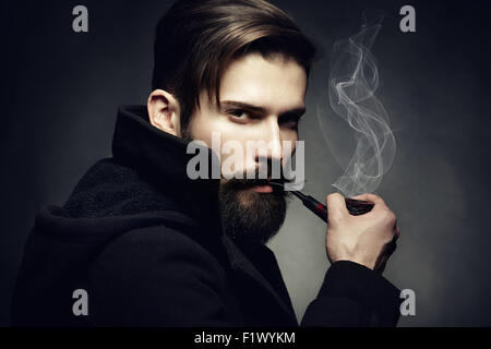 Dark artistique portrait du jeune homme magnifique. Le jeune homme fume un tube. Close up Banque D'Images