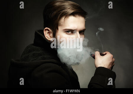 Dark artistique portrait du jeune homme magnifique. Le jeune homme fume un tube. Close up Banque D'Images