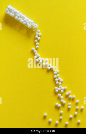 Vue aérienne de pilules homéopathiques (fait à partir de la matière inerte - sucre/lactose) Effet de déversement à partir d'une bouteille sur la surface jaune. Banque D'Images