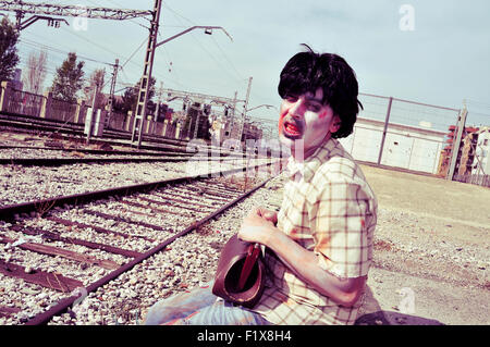 Libre d'un zombie effrayant homme portant une vieille valise attendant le train dans une gare abandonnée Banque D'Images