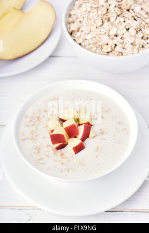 Porridge avec des tranches de pomme rouge sur une table en bois blanc Banque D'Images