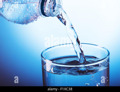 Verser de l'eau de la bouteille en verre sur fond bleu Banque D'Images