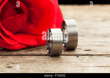 Anneaux de mariage d'argent ou de platine sur table en bois, rose rouge en arrière-plan Banque D'Images