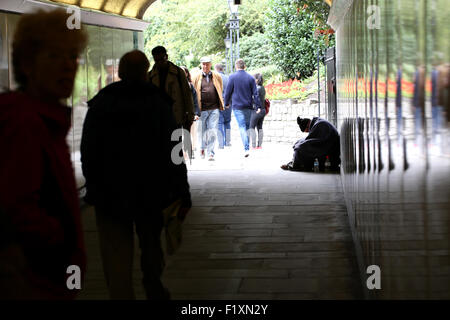 Un homme sans-abri assis à mendier mais vers le bas et dans un passage souterrain au centre de Londres comme les gens passer sur un poste occupé midi ignorant Banque D'Images