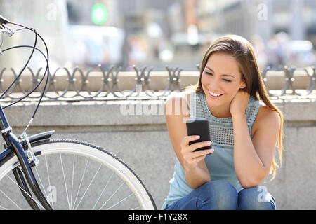 Happy girl médias dans un téléphone intelligent assis dans la rue à côté de son vélo Banque D'Images