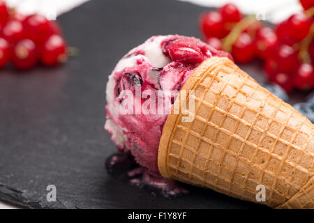 Cornet de crème glacée avec boule de fruits rouges sur fond texturé noir. Banque D'Images