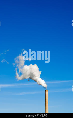 Répandant des usines polluantes blanc nuage de fumée verticalement vers le haut et gauche dans ciel bleu clair. Banque D'Images