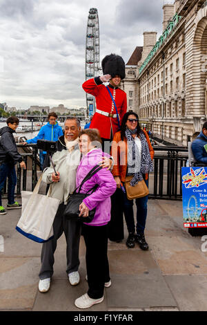 Un homme en uniforme de Garde les mains des tracts et pose pour des photos avec les touristes, Londres, Angleterre Banque D'Images