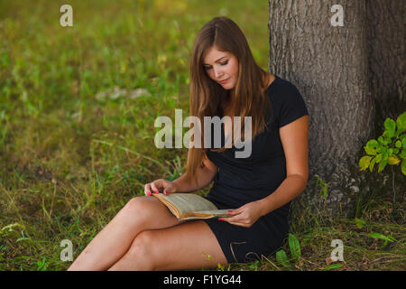 Femme fille lire un livre sous un arbre assis nature été edu Banque D'Images