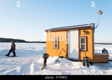 Passé une petite femme raquettes pêche dorée hutte avec une petite grille, pelle et raquettes situé au milieu d'un froz Banque D'Images