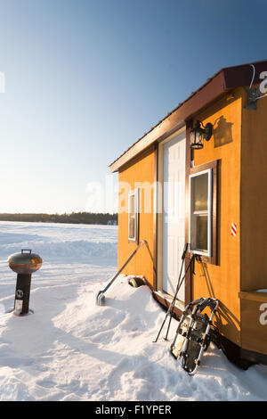 Petite cabane de pêche de couleur or avec une petite grille, pelle et raquettes situé au milieu d'un lac gelé en hiver, Banque D'Images