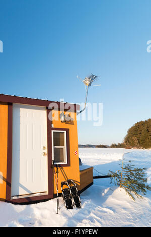 Petite cabane de pêche de couleur or avec une petite grille, pelle et raquettes situé au milieu d'un lac gelé en hiver, Banque D'Images