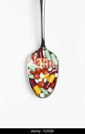 Un mélange de drogues/médicaments, comprimés et capsules sur une cuillère en appui sur une surface blanche. Banque D'Images
