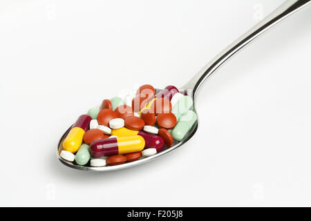 Un mélange de drogues/médicaments, comprimés et capsules sur une cuillère en appui sur une surface blanche. Banque D'Images
