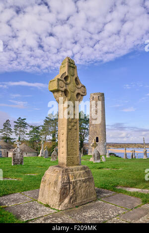 L'Irlande, dans le comté d'Offaly, le monastère de Clonmacnoise, Croix du Sud de règlement et tour ronde avec rivière Shannon en arrière-plan. Banque D'Images