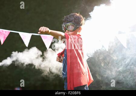 Garçon portant ces lunettes et cape de super-héros en position en face de nuage de fumée Banque D'Images