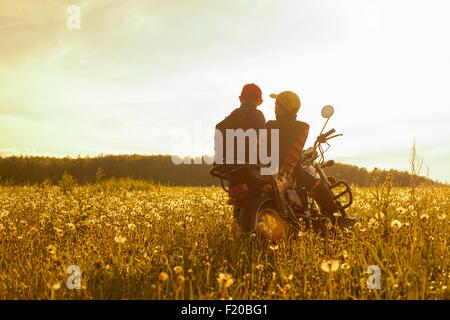 Deux jeunes garçons, assis sur moto, en champ, vue arrière Banque D'Images