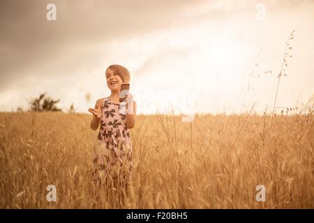 Girl using smartphone tout en riant dans champ de blé Banque D'Images