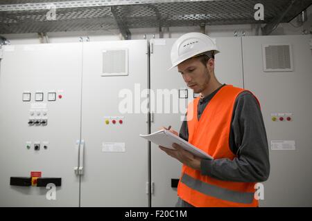 Jeune homme lecture ingénieur paperasse dans local technique Banque D'Images