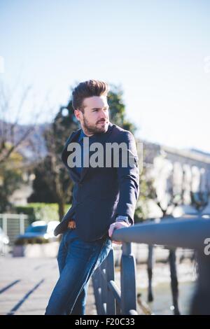 Young man leaning against railing et regardant par-dessus son épaule Banque D'Images